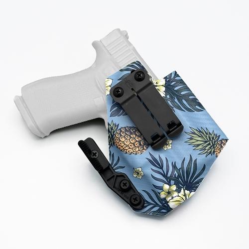 Custom Inside the Waistband (IWB) KYDEX holster for Glock 43X Rail and Glock 43X MOS with Streamlight TLR-7 sub. The holster features a tropical print with pineapples, dark palm leaves, and white flowers on a light blue Carbon Fiber background. It is equipped with a DCC Monoblock and a Modwing concealment claw